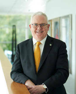 Principal wearing a black suit and smiling in a hallway.