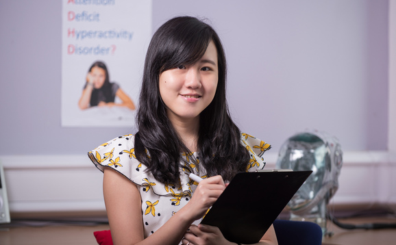 Postgraduate Taught psychology student holding clipboard with head simulator and psychology poster