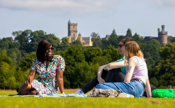 Happy students sitting in Kings Park with a Scottish castle in the background