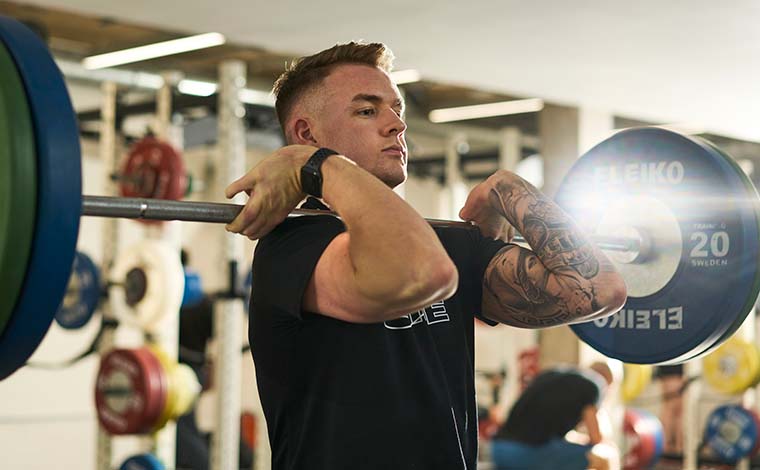 A student lifting a barbell in the university's strength and conditioning suite