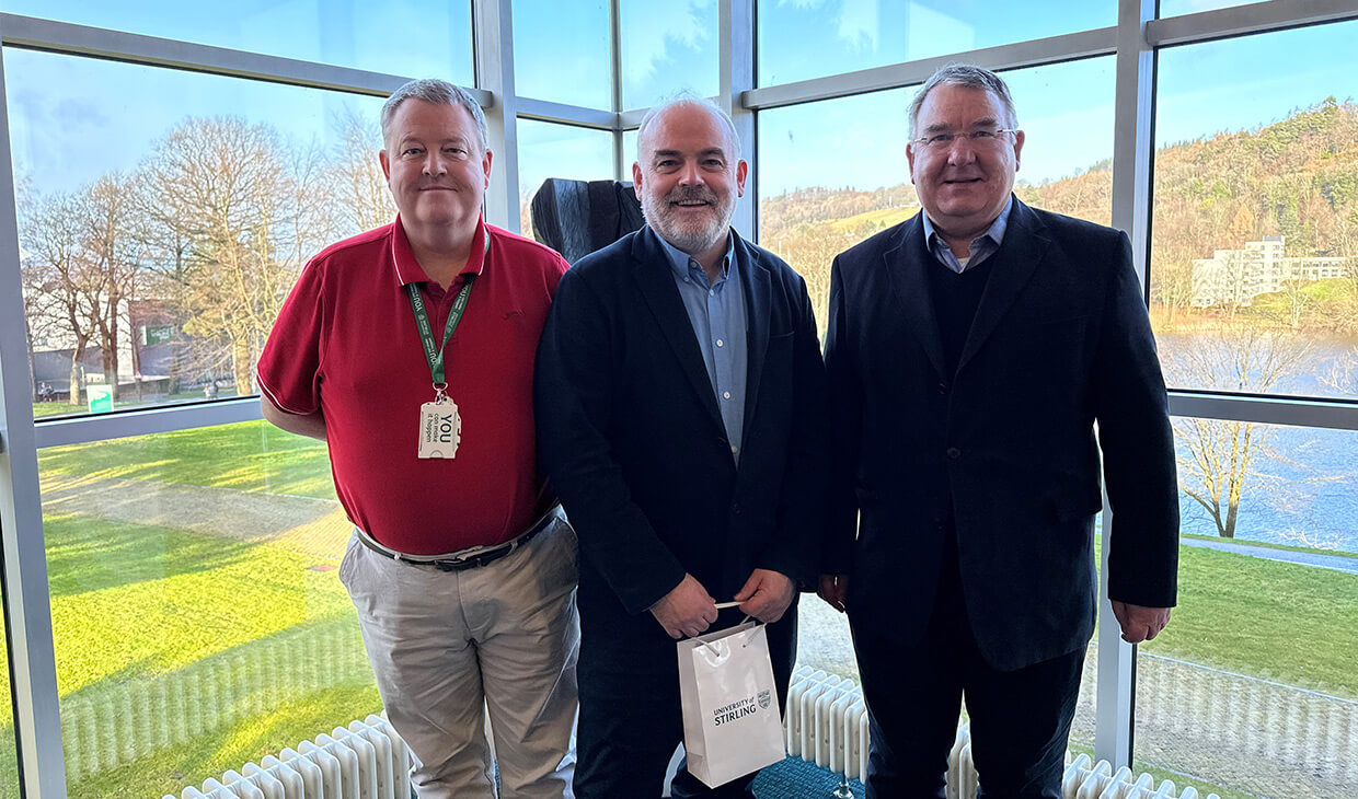 Three men pose by windows