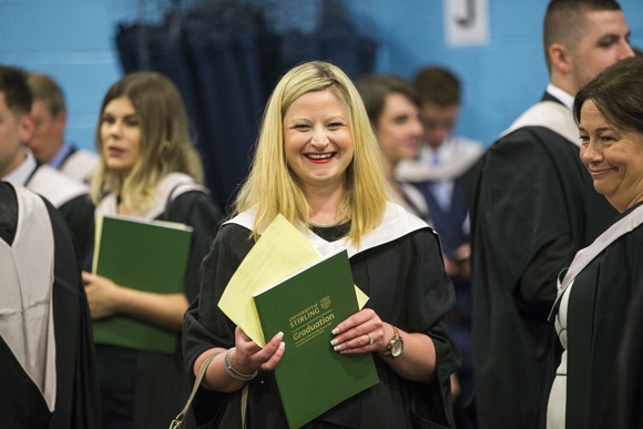 Graduate in ceremony holding graduation programme