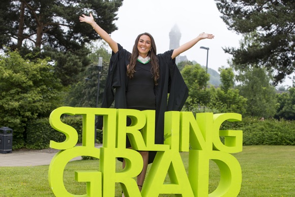 Graduate wearing gown by the loch