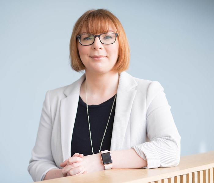 Head shot of woman wearing glasses, off-white jacket and black top