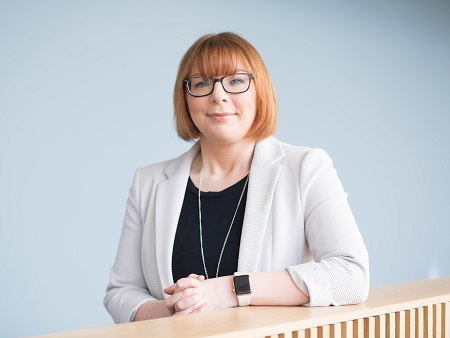 head and shoulders shot of woman wearing glasses, off-white jacket and black top