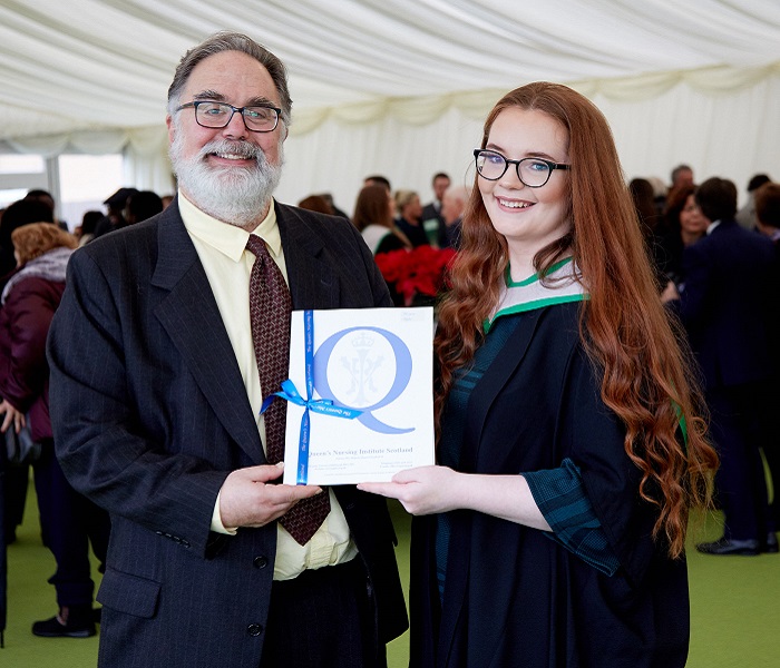 man with beard presenting award to woman in graduation robe