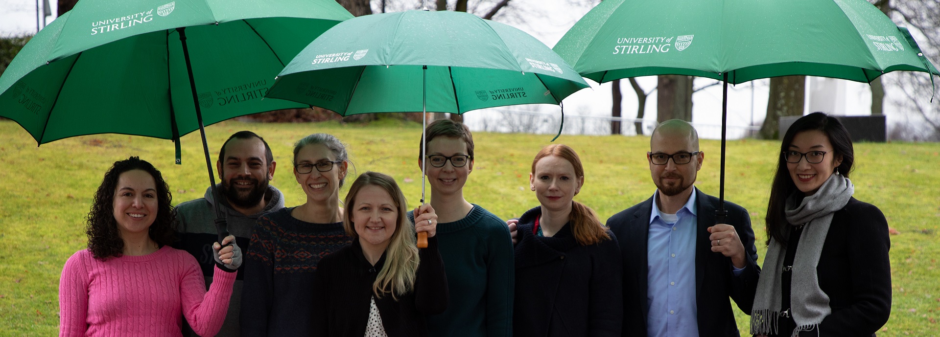 Group of eight people standing under three University umbrellas