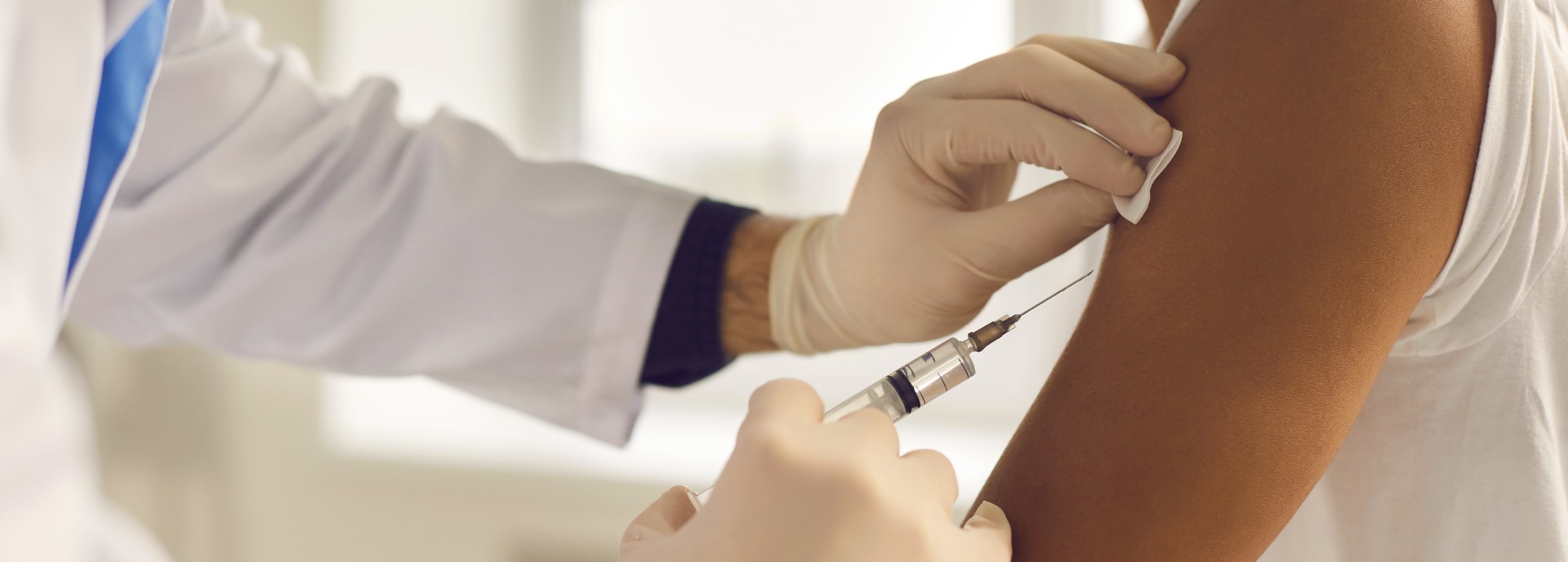 Doctor in medical gloves giving vaccine jab to a patient. Close-up of hands holding syringe and cleaning skin on upper arm before antiviral injection