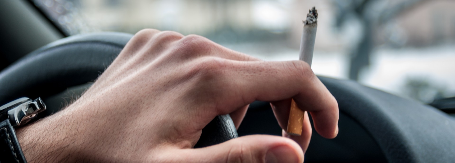 Image of driver's hand on wheel with cigarette