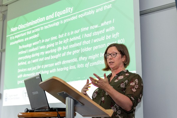 Dr Louise McCabe, Senior Lecturer in Dementia and Ageing, gives a presentation on the Technology and Social Connectedness project. She stands at a lectern in front of a power point presentation.