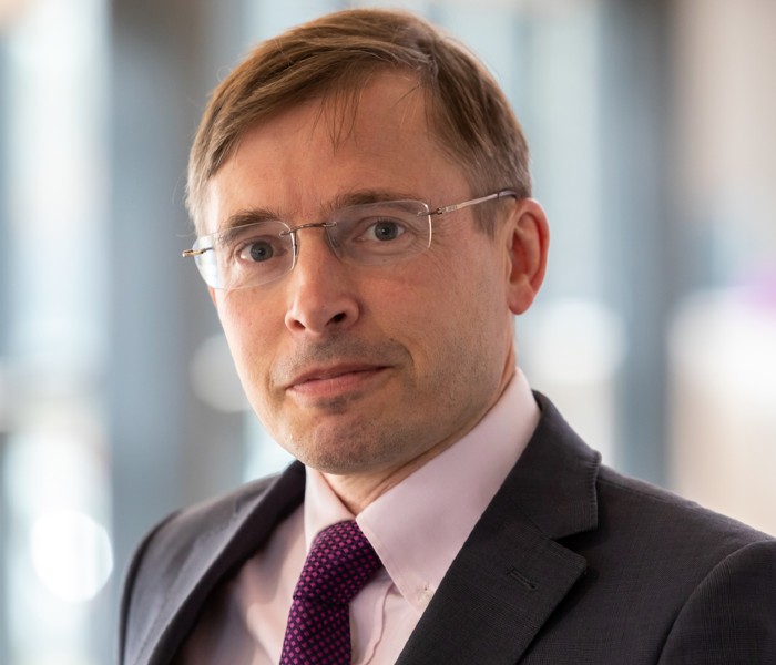 Portrait photograph of Neville Wylie. He wears a suit, short and tie, glasses.