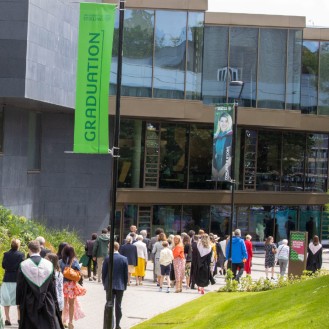 Graduates in robes walking by Campus Central