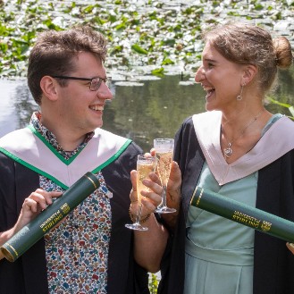 Two graduates holding scrolls in front of the loch