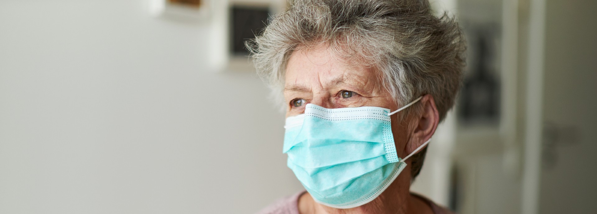 Older person wears a mask and is gazing out of a window