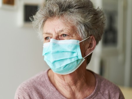 Older person wears a mask and is gazing out of a window