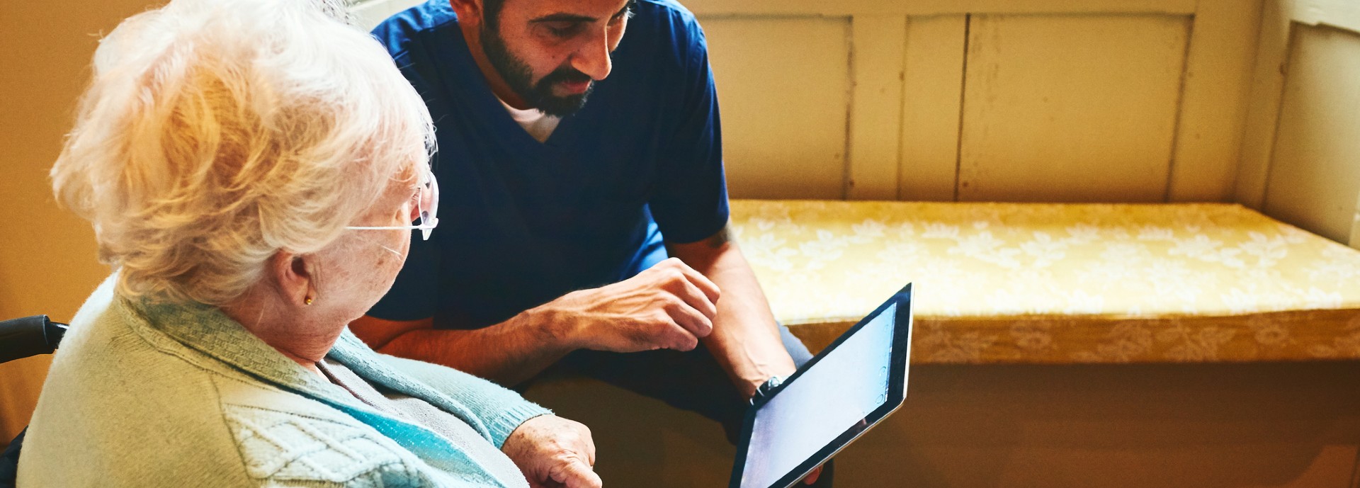 Healthcare worker with senior woman using digital tablet at care home