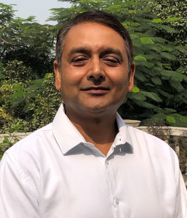 Photograph of Rohit Jaiswal. He is photographed outside, with greenery in the background and is wearing a white shirt.