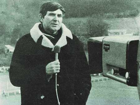 A black and white photograph of the late Rugby Union commentator Bill McLaren holding a microphone