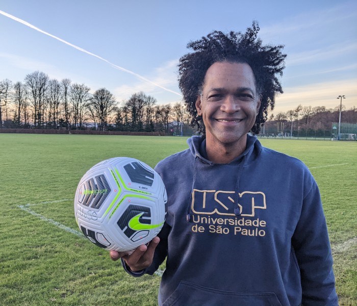 Donald Silva stands on a football pitch holding up a football