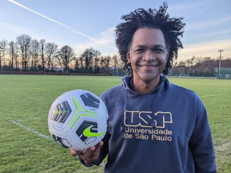 Donald Silva stands on a football pitch holding up a football