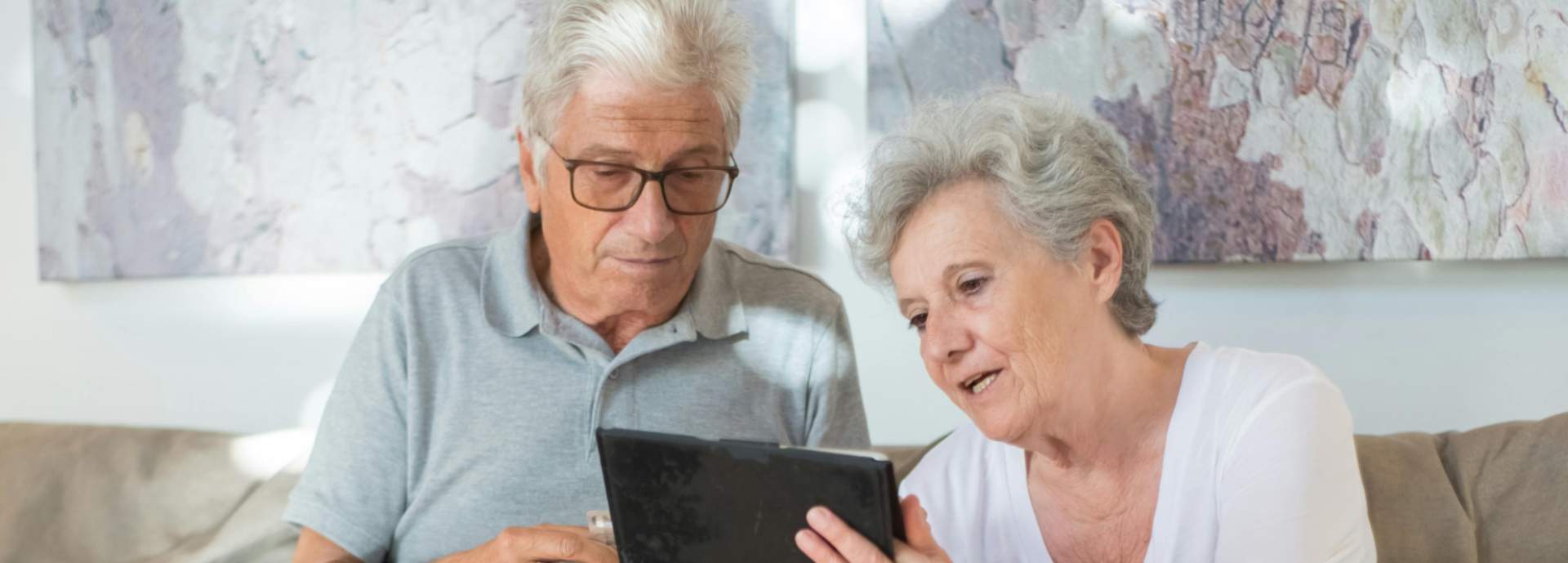 older man and woman with tablet on sofa