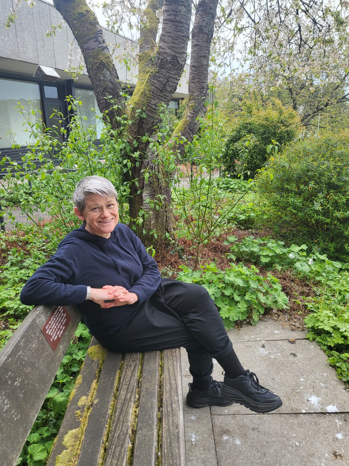 Audrey sitting on a bench in a garden with a tree behind them