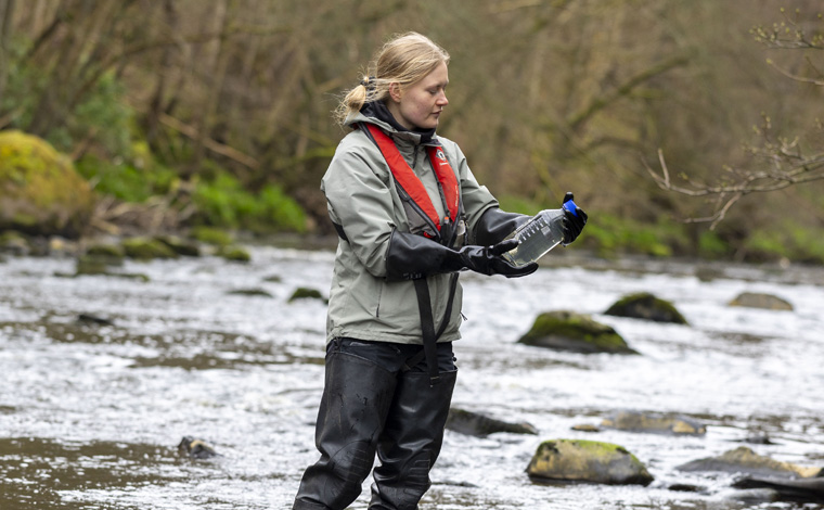 academic in river analysing a water sample