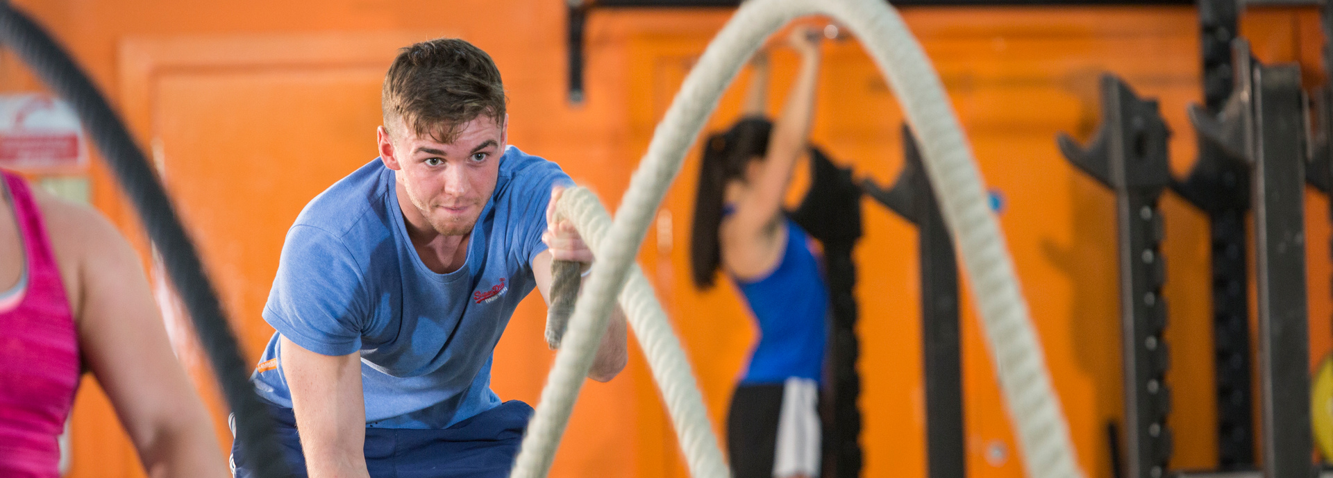 Man in blue top using rope in exercise class with orange wall