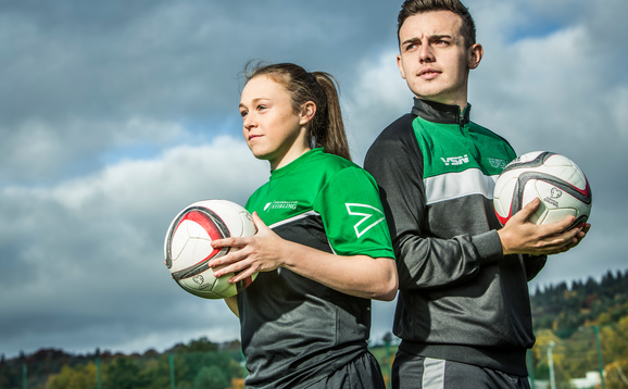 Man and woman in sports clothes posing with footballs