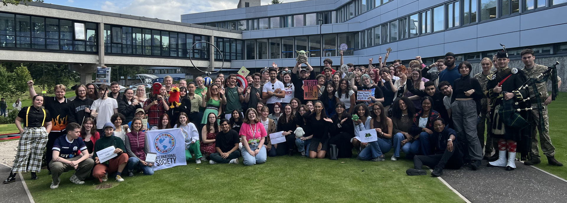 Large group of students gathered outside holding signs for their societies