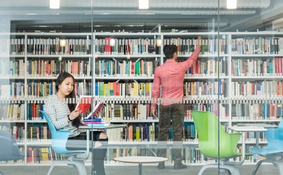 Two students reading books in the library